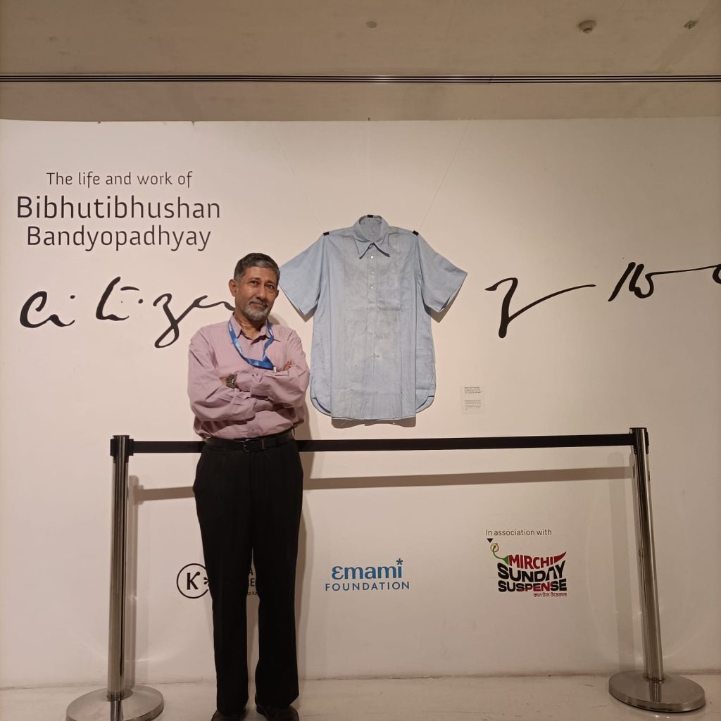 বিভূতিভূষণ-৩। প্রদর্শনীর শুরুতেই দেওয়ালে শৈল্পিক আঙ্গিকে লেখা ‘পথ বেঁধে দিল বন্ধনহীন গ্রন্থি’ কথাটা। ইংরেজিতে ‘The slipknot-fastened path’. আর ডান দিকের দেওয়ালে ‘পথের কবি’-র নিজস্ব সেই পরিধান।